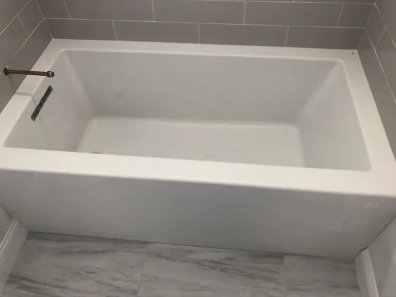 Alcove bathtub installation in progress with starting gray subway tile surround and marble-look floor by A.J. LeBlanc Heating in a Southern NH bathroom