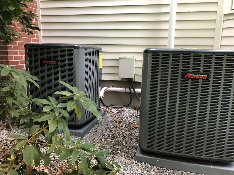 Dual Amana central air conditioners installed beside a brick home by A.J. LeBlanc Heating in Southern NH