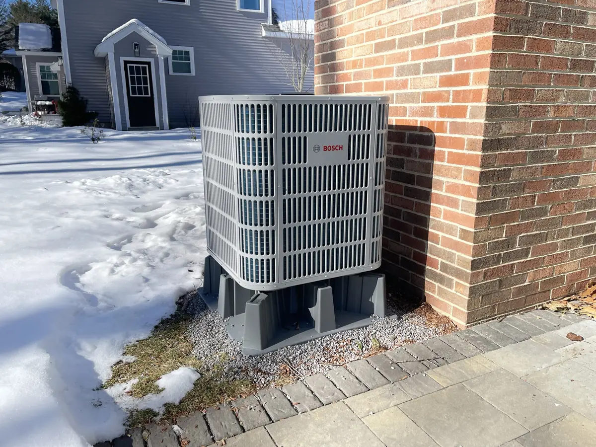 Bosch cold-climate outdoor heat pump installation against a brick home in Southern NH during winter