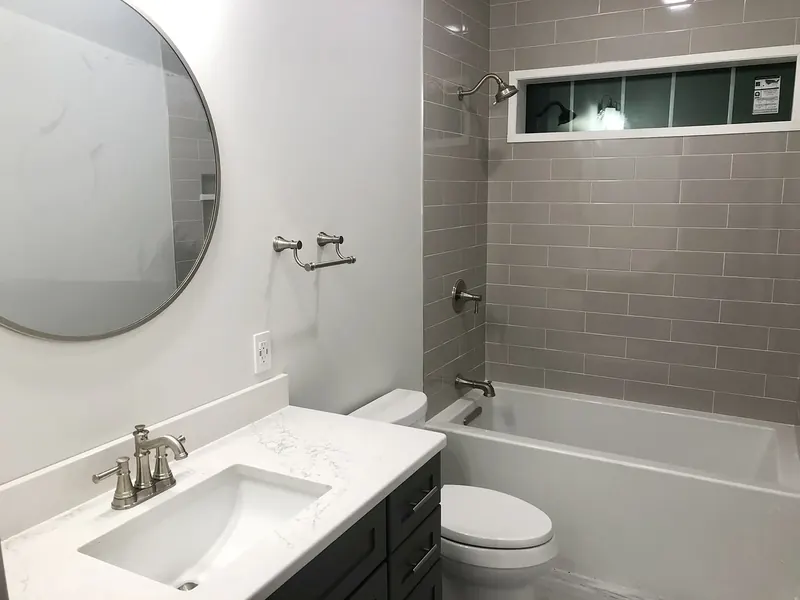 Bathroom with brushed nickel widespread faucet, undermount sink, white marble vanity, round mirror, and matching brushed nickel shower head and tub spout over gray subway tile by A.J. LeBlanc Heating in Southern NH
