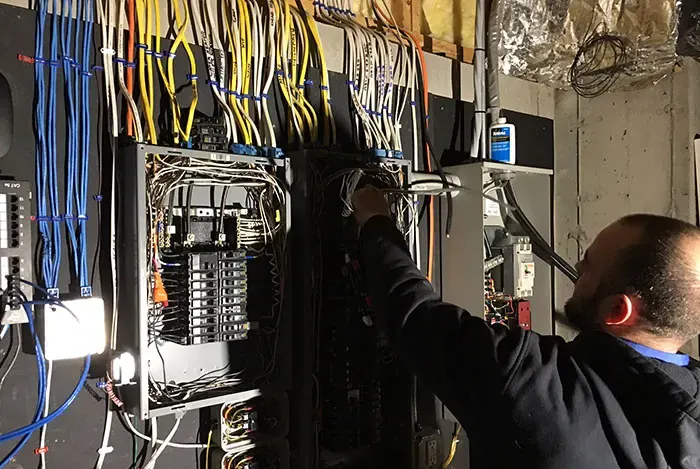 A.J. LeBlanc Heating licensed electrician wiring a 200-amp main panel, generator transfer switch, and sub-panel in a Southern NH home