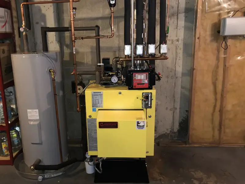 Energy Kinetics System 2000 oil boiler with multi-zone copper manifold next to a tank water heater in a Southern NH basement