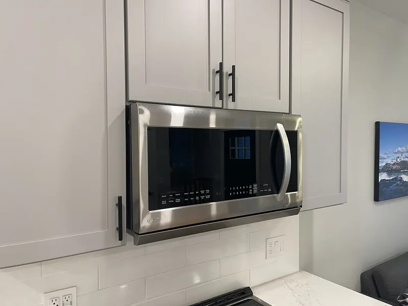 GE stainless steel over-the-range microwave installed between white shaker cabinets with subway tile backsplash by A.J. LeBlanc Heating in a Southern NH kitchen