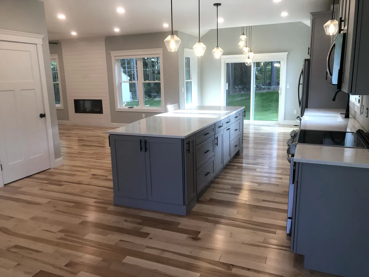 Open-concept Southern NH kitchen with three pendant lights over the island and recessed ceiling lighting installed by A.J. LeBlanc Heating