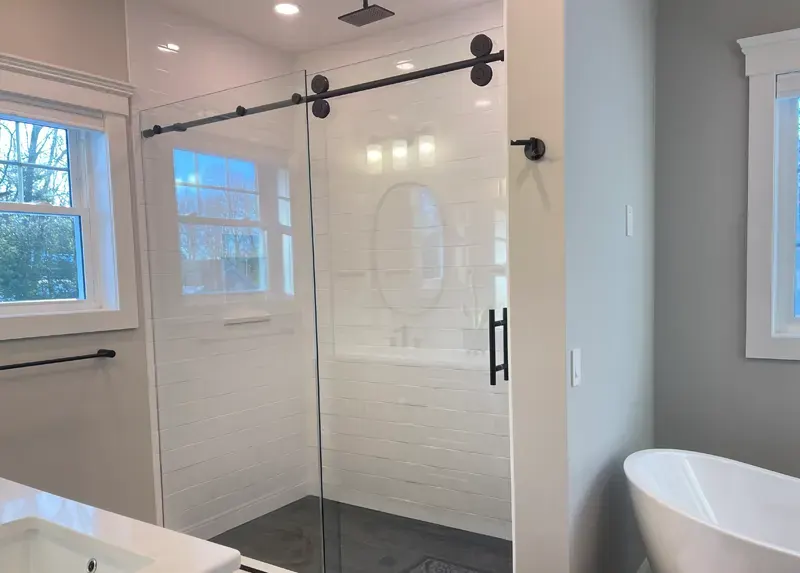 Large subway tile shower with frameless glass barn door installed by A.J. LeBlanc Heating in a Southern NH home