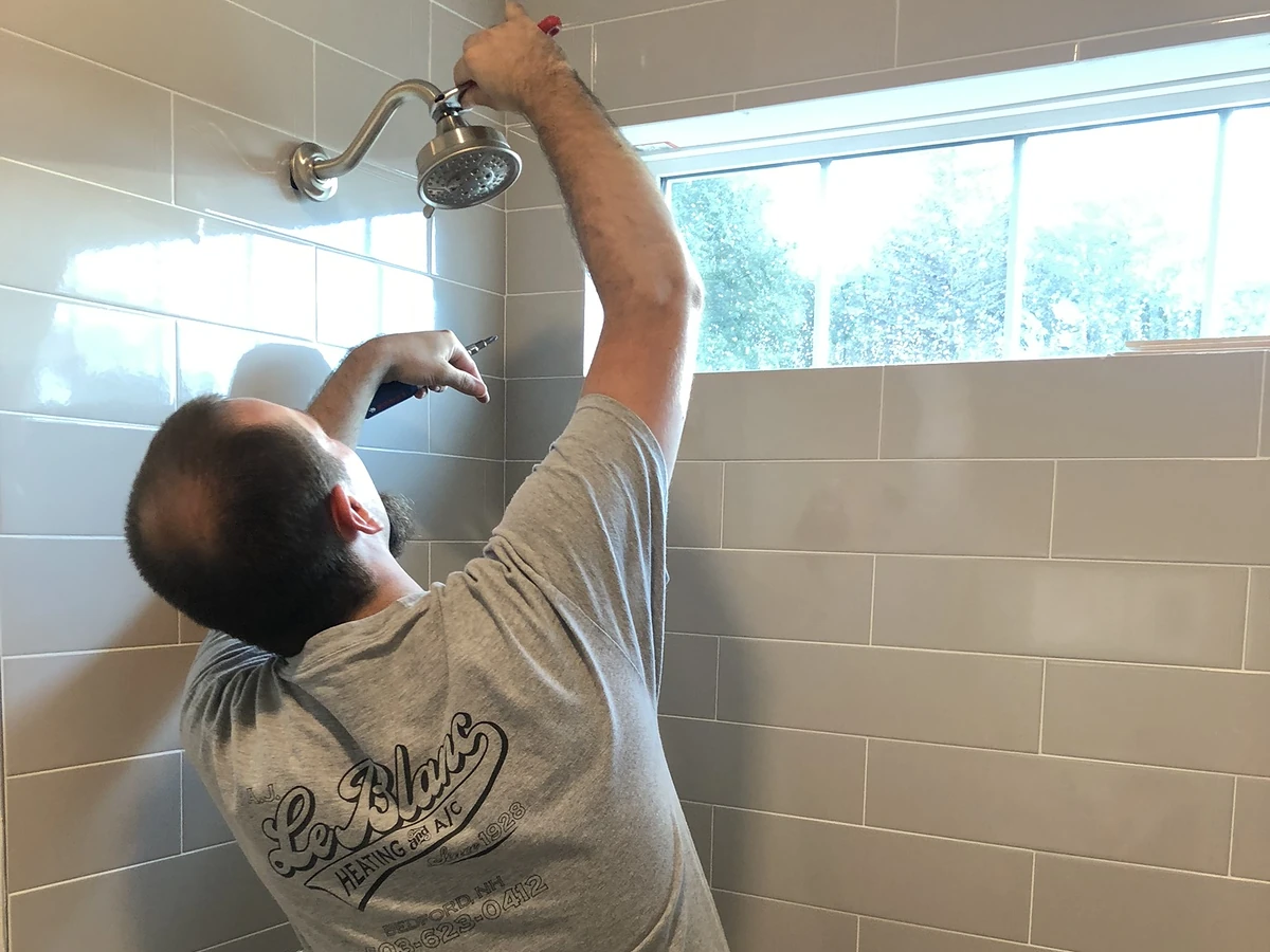 A.J. LeBlanc Heating master plumber installing a brushed nickel showerhead in a new gray subway tile shower in a Southern NH home