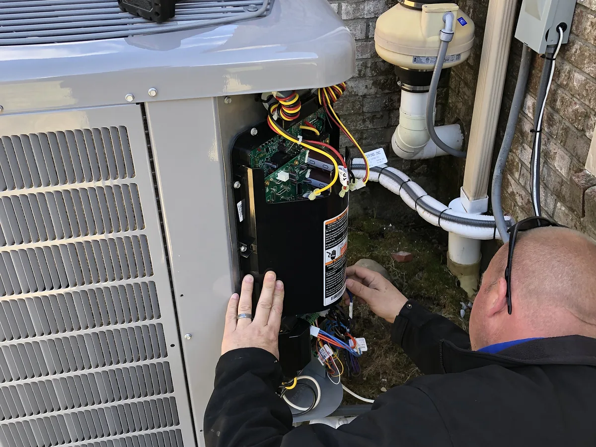 A.J. LeBlanc Heating technician servicing the electrical control compartment of an outdoor condenser unit at a Southern NH home during a Rate Lock maintenance appointment
