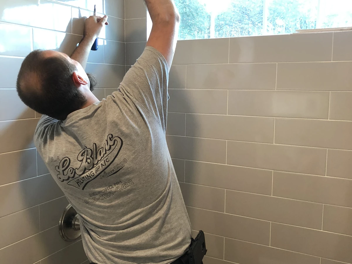 A.J. LeBlanc Heating master plumber installing a shower head in a new gray subway tile shower in a Southern NH home