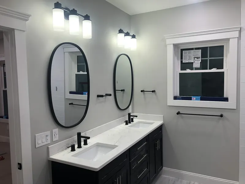 Double-vanity bathroom with two matte black single-handle faucets, undermount sinks, white quartz counter, black shaker cabinets, oval mirrors, and cylindrical wall sconces by A.J. LeBlanc Heating in Southern NH