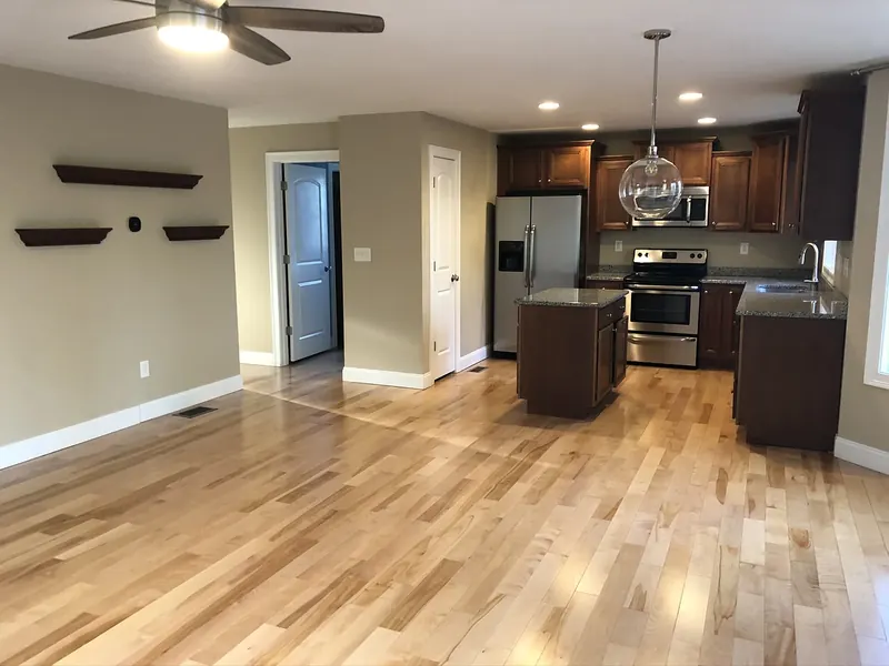 Open-concept kitchen and living room with ceiling fan, glass globe pendant over the island, and recessed LED ceiling lighting installed by A.J. LeBlanc Heating in a Southern NH home