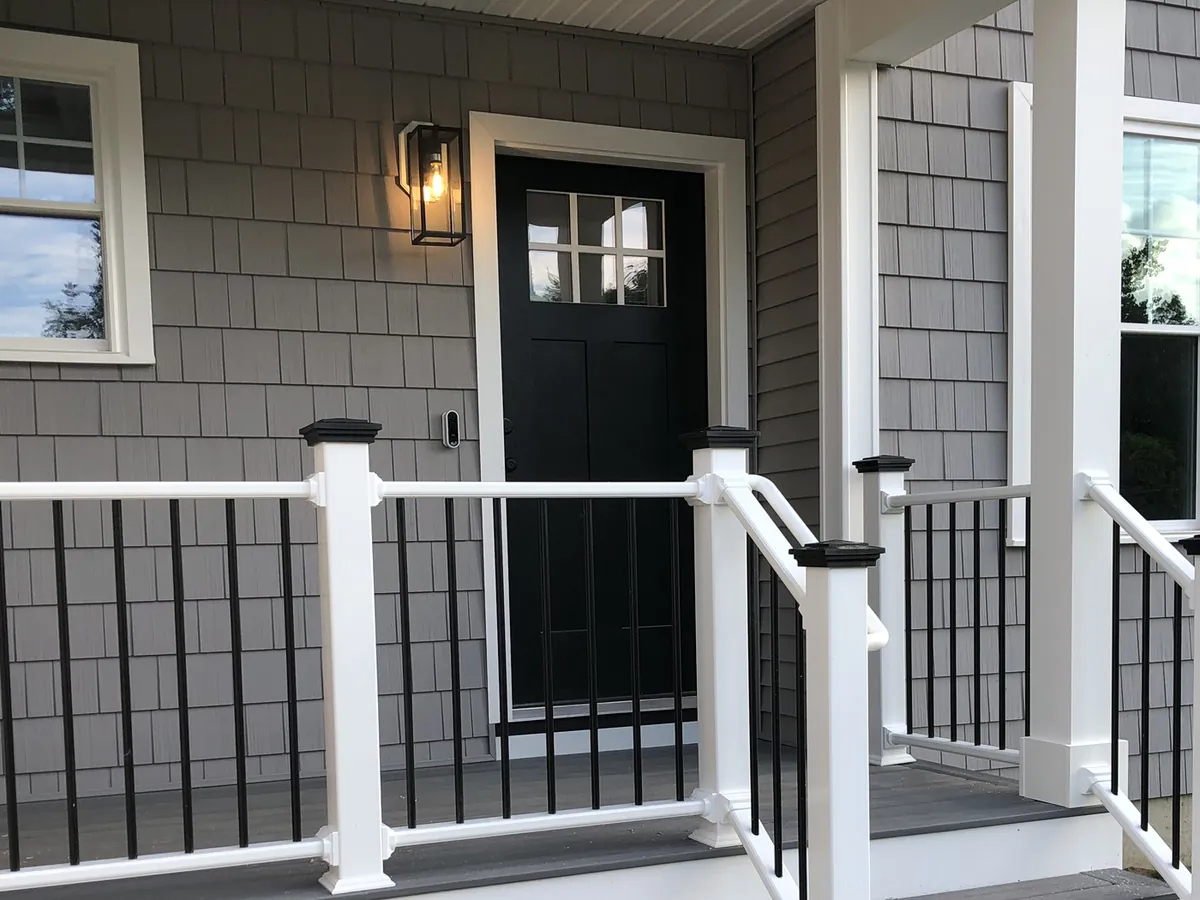 Front porch entry lighting installation in Southern NH with a wall-mounted lantern sconce beside a black entry door and post-cap lights along the railing, installed by A.J. LeBlanc Heating