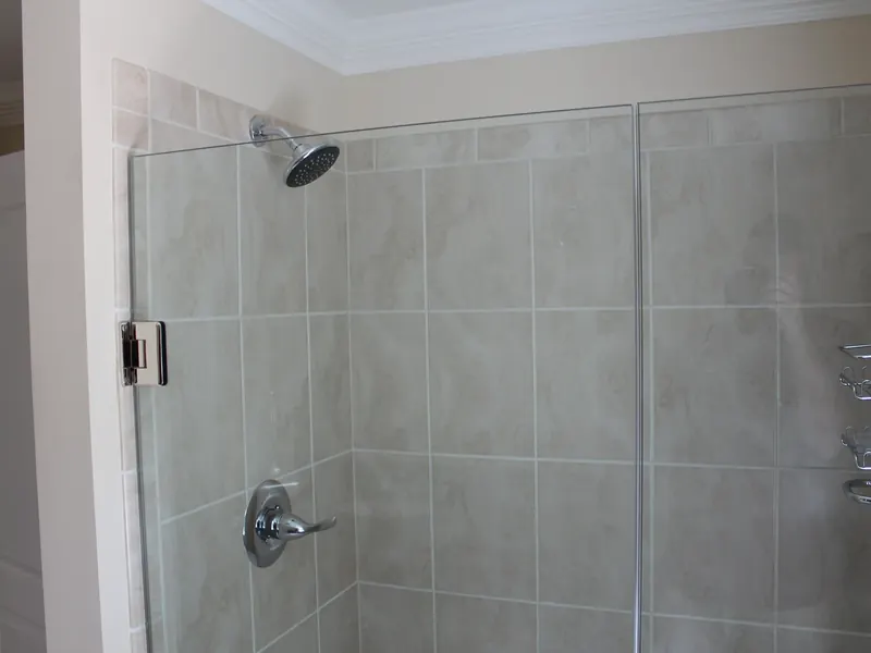 Ceramic tile shower with chrome showerhead and handheld behind a frameless glass door installed by A.J. LeBlanc Heating in a Southern NH home