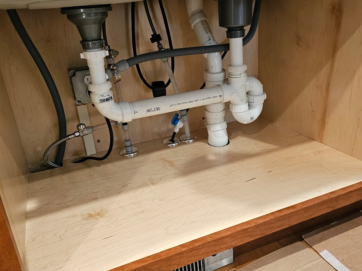 Under-sink plumbing replacement under a double-bowl kitchen sink with new PVC trap and supply valves by A.J. LeBlanc Heating master plumbers in a Southern NH home
