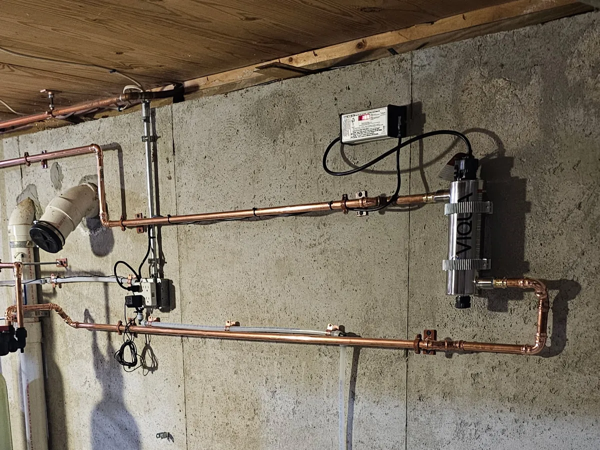 Viqua UV water sterilizer mounted vertically on a concrete wall with copper plumbing and control box in a Southern NH mechanical room, installed by A.J. LeBlanc Heating